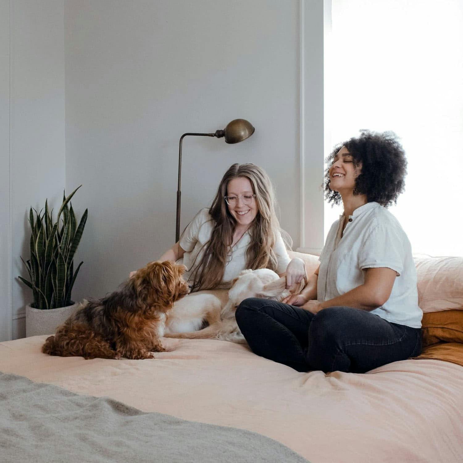 Image of two women on the bed with dog, looking happy.
